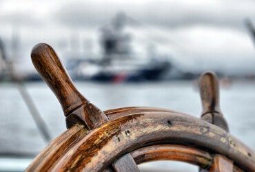 Ein hölzernes Steuerrad vor einem Schiff.